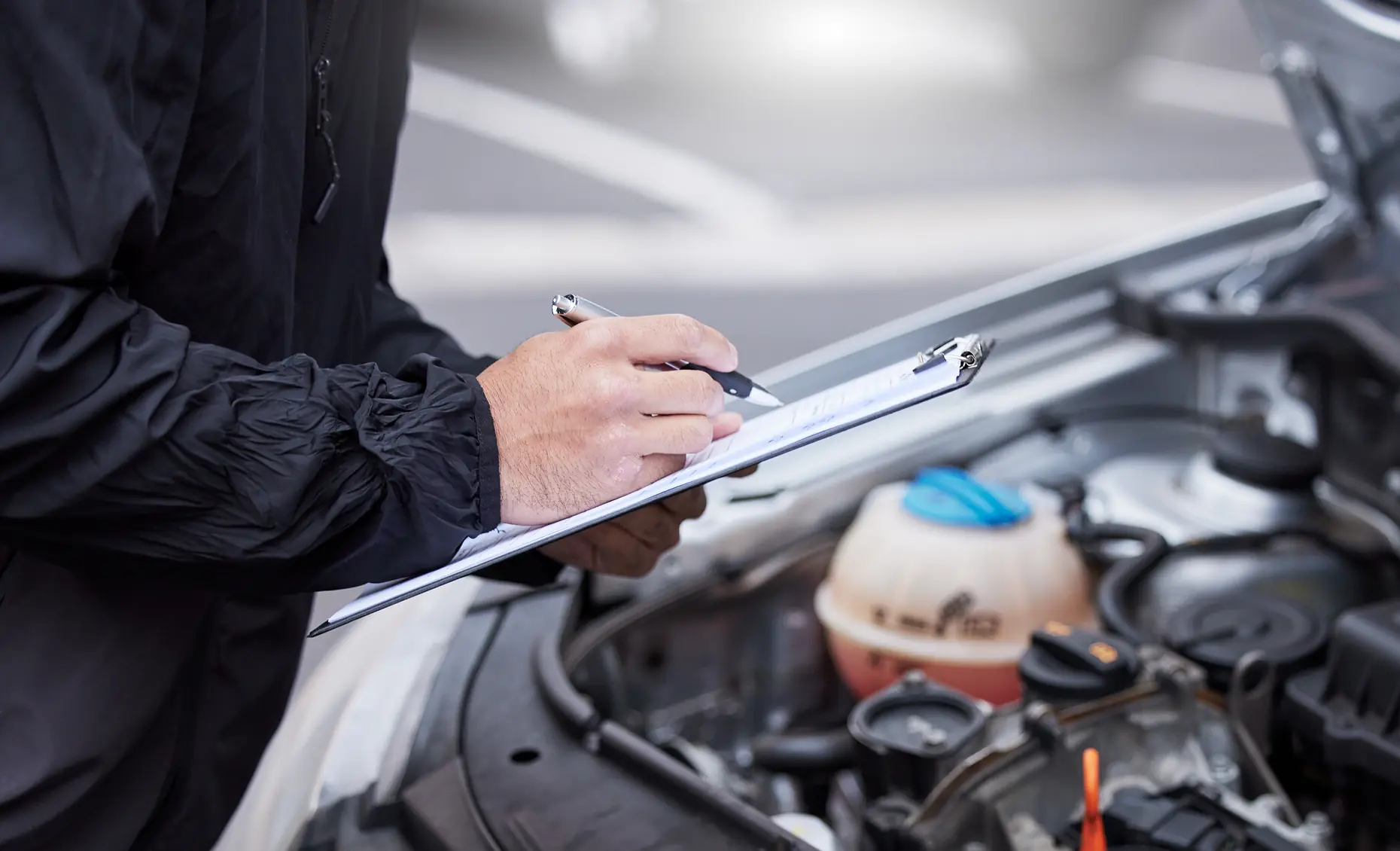 Vehicle inspections in Albuquerque, NM by Albuquerque Auto Repair and Tire. Image of a technician documenting findings on a clipboard over an open engine bay, emphasizing safety and reliable performance.
