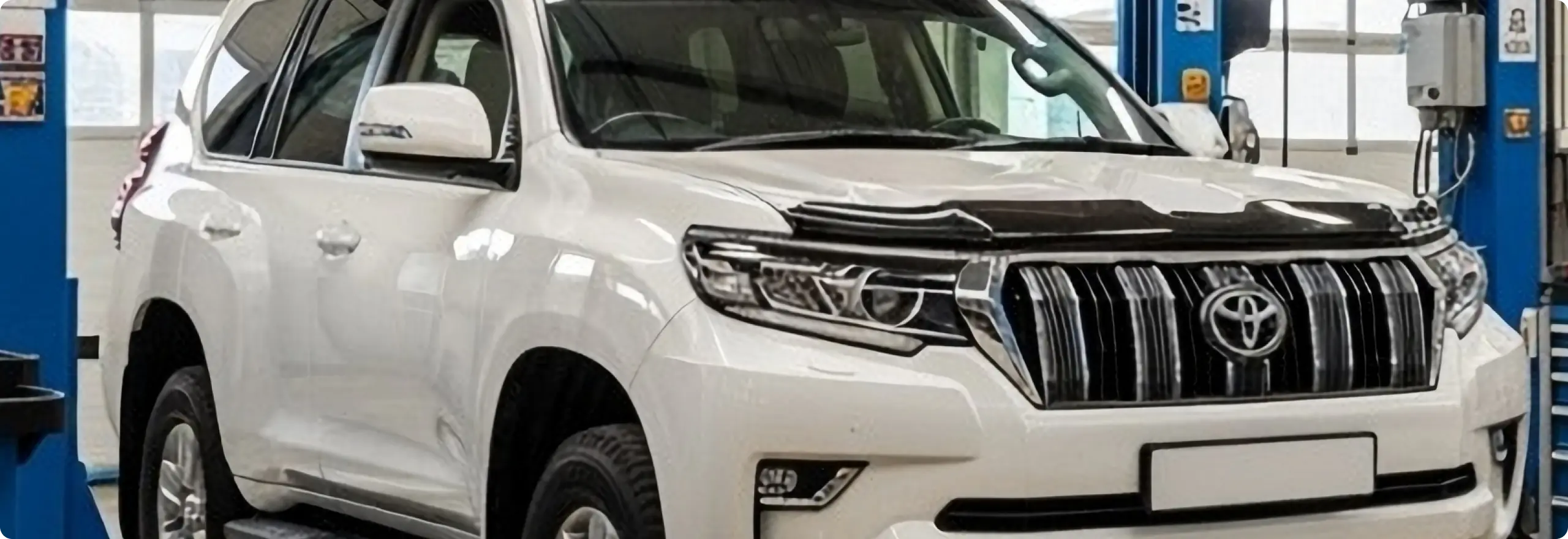 White Toyota SUV on lift inside an auto repair shop.
