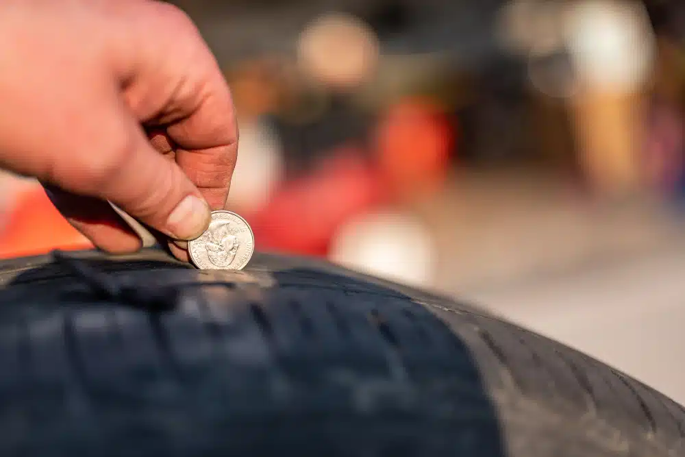 Tire tread depth, tire services in Albuquerque, NM by Albuquerque Auto Repair and Tire. Image showing a mechanic using a coin to measure tread depth on a worn tire, emphasizing the importance of regular tire checks for safety and performance.